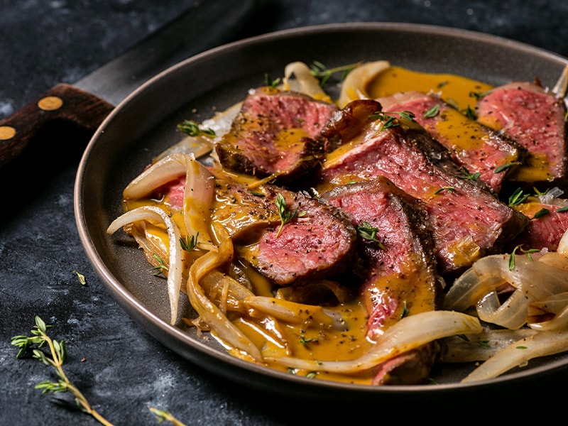 Close up of sliced rare steak and onion sizzling in a frying pan