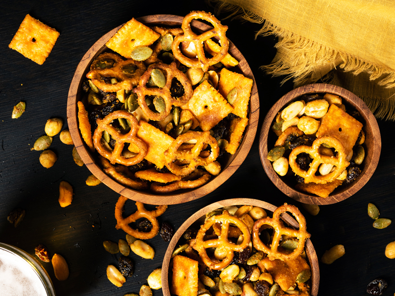 Overhead photo of three bowls filled with pretzels, nuts, crackers and seeds