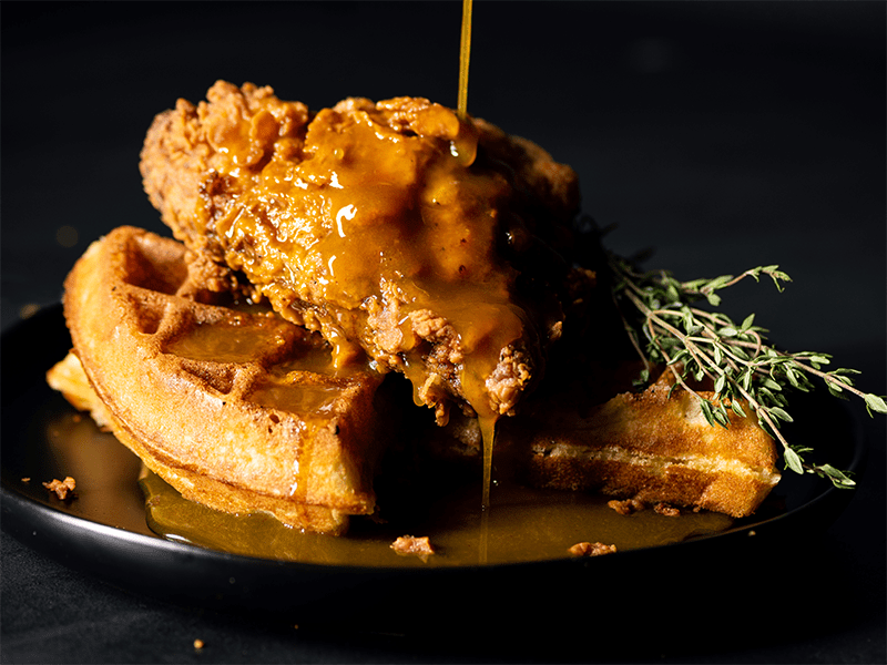 Hot Mustard Maple Syrup being drizzled onto a plate of chicken and waffles