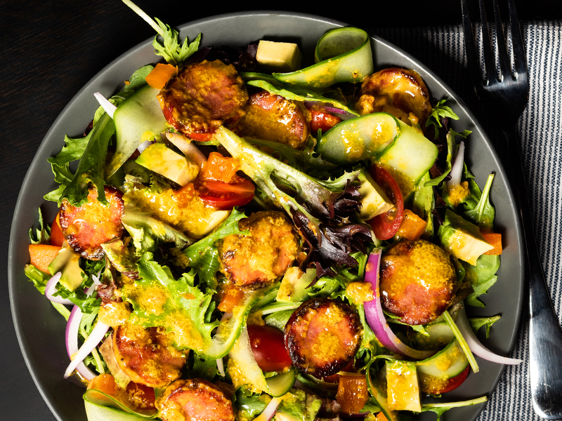 Overhead photo of a salad bowl filled with veggies and slices of grilled sausage