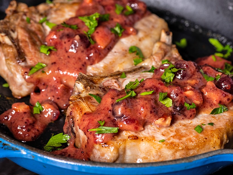 Close up of pork chops on a plate, drizzled with cranberry mustard sauce