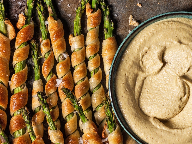Dipping sauce in a bowl next to bread-wrapped asparagus